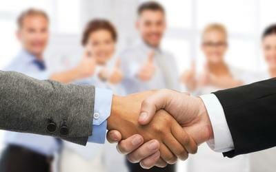 Why Use a Health Insurance Agent? Two men in suits shaking hands with five people looking on.
